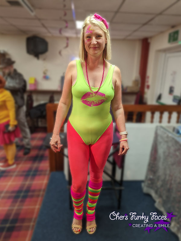 Lady in yellow neon leotard with pink neon tights and multicoloured neon leg warmers has pink glitter zig zag over her eye Chers Funky Faces