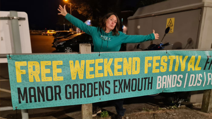 Tash Funky Punky with arms outstretched above ManorFest Banner at night