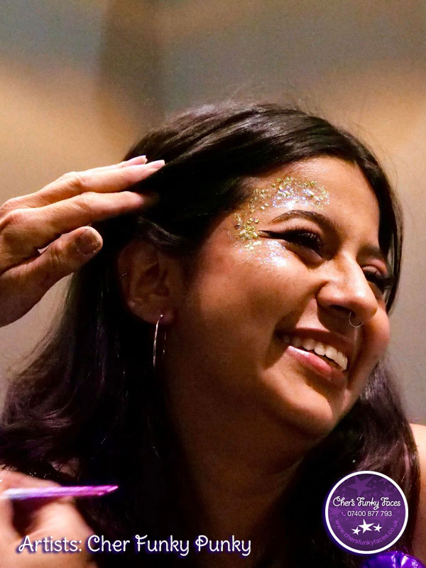 Student smiling as their face get festival glitter applied