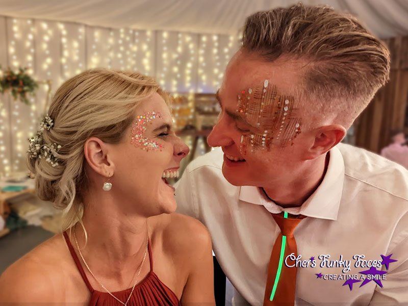 Couple laughing with festival style face paint and glitter at wedding reception Trevenna Chers Funky Faces